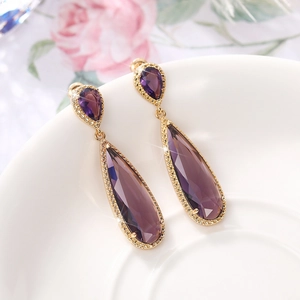 Elegant gold drop earrings with teardrop purple crystals on a white ceramic plate