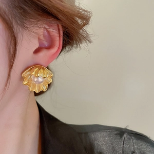 Detailed close-up of a vintage golden shell earring featuring a central white pearl inlay