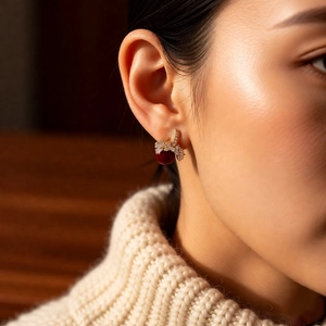 Detail of 18k gold plated earring with red gemstone and sparkling floral bow stud