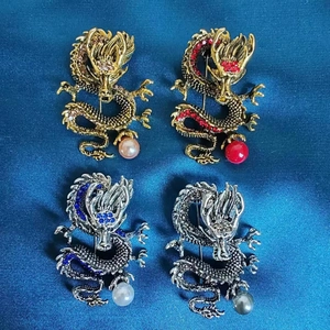 Detail von vier Drachen-Broschen mit Strass und Perlen auf blauem Seidenhintergrund