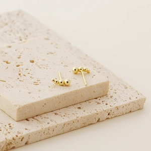 Detailed view of minimalist gold stud earrings with three graduated beads on a stone base