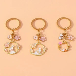 Detailed view of three enamel flower wreaths featuring white cat and rabbit charms with gold chains