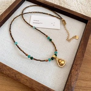 Detail of tiger eye bead necklace with gold gourd pendant on rustic linen background