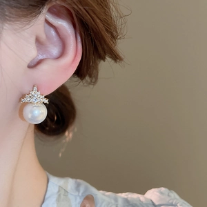 Detailed view of elegant crown earrings with gold zircons and a round white pearl charm