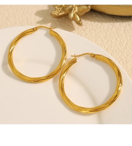 Detail shot of gold-plated twisted hoop earrings on a ceramic tray with a warm backdrop