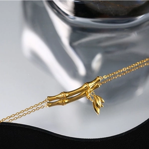 Minimalist 18k gold bamboo joint necklace featuring leaf pendants and mirror reflection