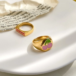 Detail of gold cherry enamel ring and Howdy letter signet ring on white plate