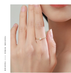 Detail of a gold beaded ring featuring a pear-shaped clear gemstone worn on a finger