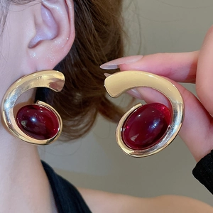 Detail of large C-shaped gold-tone earrings with oval purple-red resin gemstone