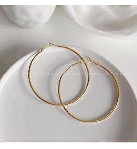 Close-up of minimalist gold hoop earrings placed on a white ceramic plate and silk cloth
