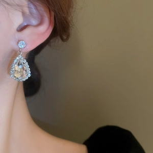 Close-up of elegant silver teardrop crystal earrings with small diamond-like accents on ear