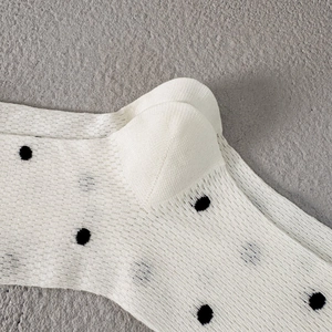 Close-up of breathable white mesh socks with black polka dots and fine knit texture