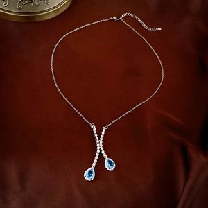 Vue détaillée du collier argenté en Y avec zircons bleus en goutte sur velours sombre