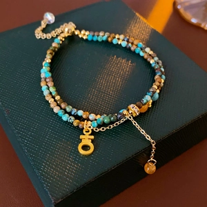 Détail d'un bracelet double couche en perles turquoise avec breloques dorées sur boîte