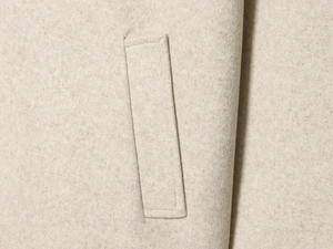 Macro shot of the beige wool fabric texture and welt pocket detail on the French style coat