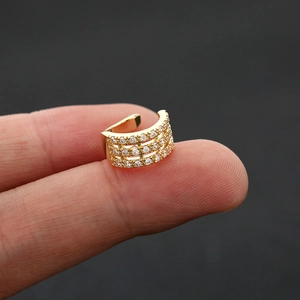 Macro shot of gold ear cuff with three rows of sparkling zircons held by hand