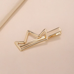 Minimalist golden crown shaped metal hair clip with polished finish on beige fabric