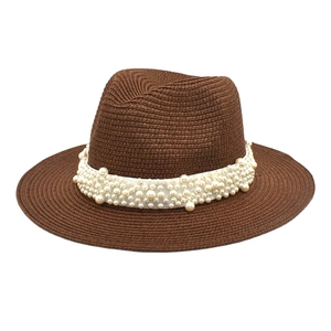 Detail view of brown woven straw fedora featuring a white ribbon and faux pearl embellishments