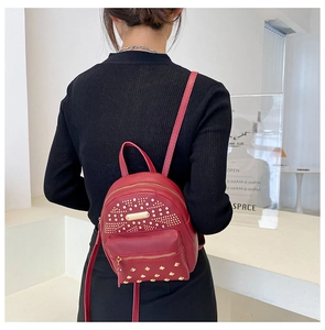 Mini red punk backpack with gold rivets and headphone jack shown on model back