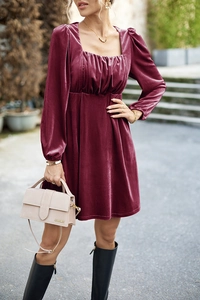 Detail van wijnrode fluwelen jurk met vierkante halslijn en een beige luxe handtas