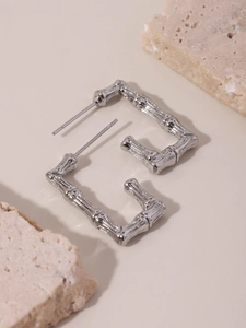 Detail of silver bamboo texture square earrings on minimalist stone pedestal