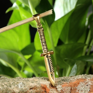 Detail of a vintage gold dagger pendant hanging on a twig over a rustic red brick