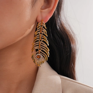 Détail de longues boucles d'oreilles plumes dorées avec strass portées par un mannequin