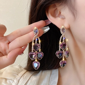 Primo piano dettagliato di lussuosi orecchini lunghi in cristallo viola con strass brillanti.