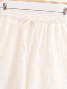 Detail of white pleated shorts featuring an elastic waistband and matching drawstring