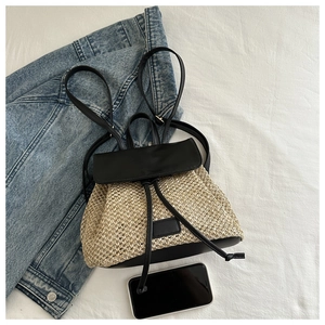 Vue à plat d'un sac à dos en paille avec garniture en cuir sur fond de tissu coton