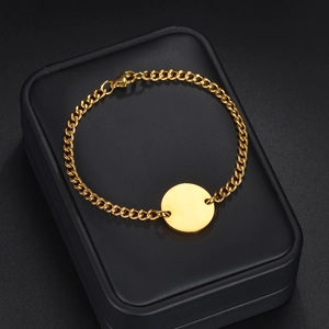 Polished gold stainless steel cuban link bracelet with engravable round tag on a jewelry box
