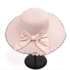 Detail of pink straw hat featuring a golden striped bow and black wavy scalloped edges