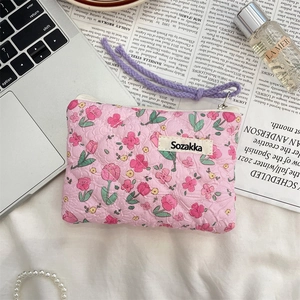 Flat lay of floral quilted storage bag with zipper and wrist strap on a stylish desk