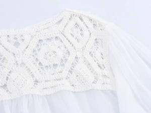 Close-up of elegant crochet hollow-out detailing and chiffon texture on white long sleeve top