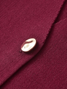 Macro view of a textured gold button on burgundy knit fabric with clean stitching
