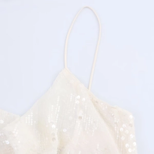 Détail de la robe caraco à paillettes crème avec fines bretelles et disques brillants