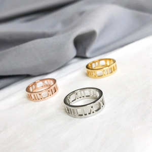 Close-up of gold, rose gold and silver Roman numeral hollow rings on fabric