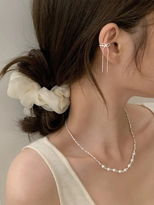 Detail of silver bow ear cuff with long tassels and pearl necklace on model