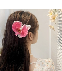 Detail of pink orchid hair clip with pearl accent on brown wavy hair for women
