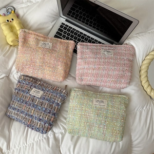 Flat lay of tweed makeup bags in pink, orange, blue, and green on white bedding
