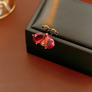 Detail of vintage enamel bee brooch with red teardrop gemstones on a black box