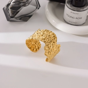 Dettaglio di un bracciale rigido dorato martellato con texture effetto lavico