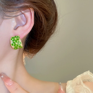 Detail view of a C-shaped gold earring with green enamel flower petal texture on a model