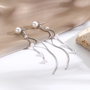 Detailed close-up of long silver fringe earrings with white pearls on silk background