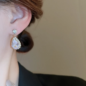 Close-up of gold pear-shaped teardrop earrings with crystals worn by a model