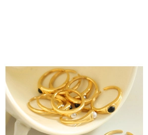 Dettaglio di anelli dorati con perle bianche e pietre nere in una tazza di ceramica