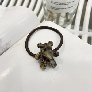 Detail of cute bear-shaped tortoiseshell hair tie with golden lettering on white background