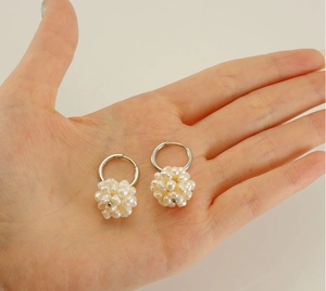Détail de créoles plaquées or 18k avec grappes de perles blanches présentées dans une main