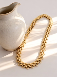 Detail of a chunky gold watch link necklace with OT buckle and artistic light shadows