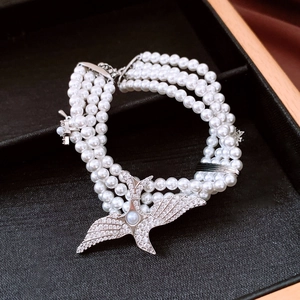 Detailed macro of a multi-layer pearl bracelet featuring a crystal-encrusted eagle clasp